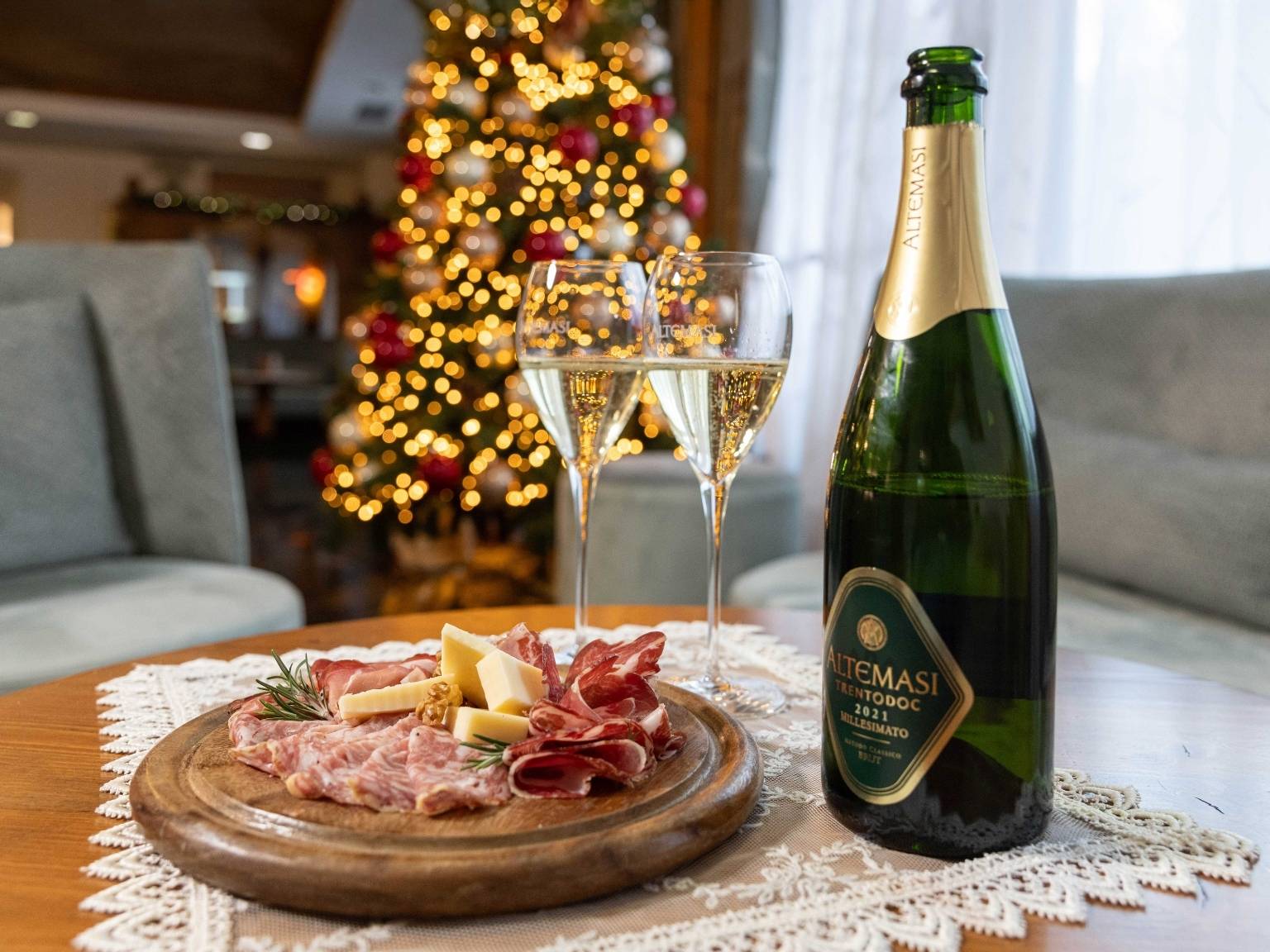 New Year's Eve toast with Altemasi Trentodoc sparkling wine and a platter of cold cuts at Hotel La Perla, with an illuminated Christmas tree in the background.